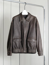 Brown leather jacket hanging on a rack against a white wall